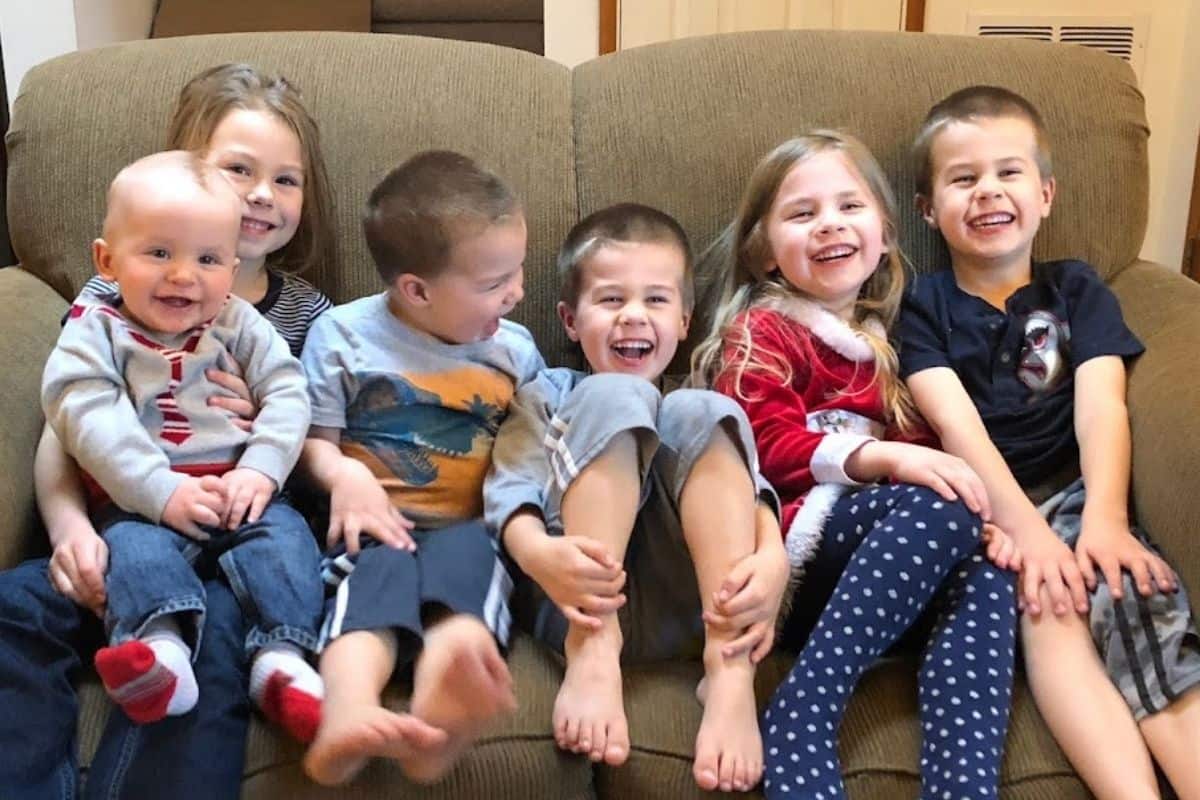 Six young children sitting on a couch having a great time laughing and smiling.