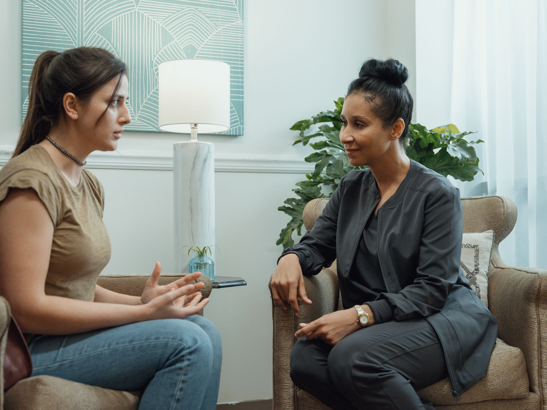 A female mental health professional sits in a chair and listens to distressed young woman