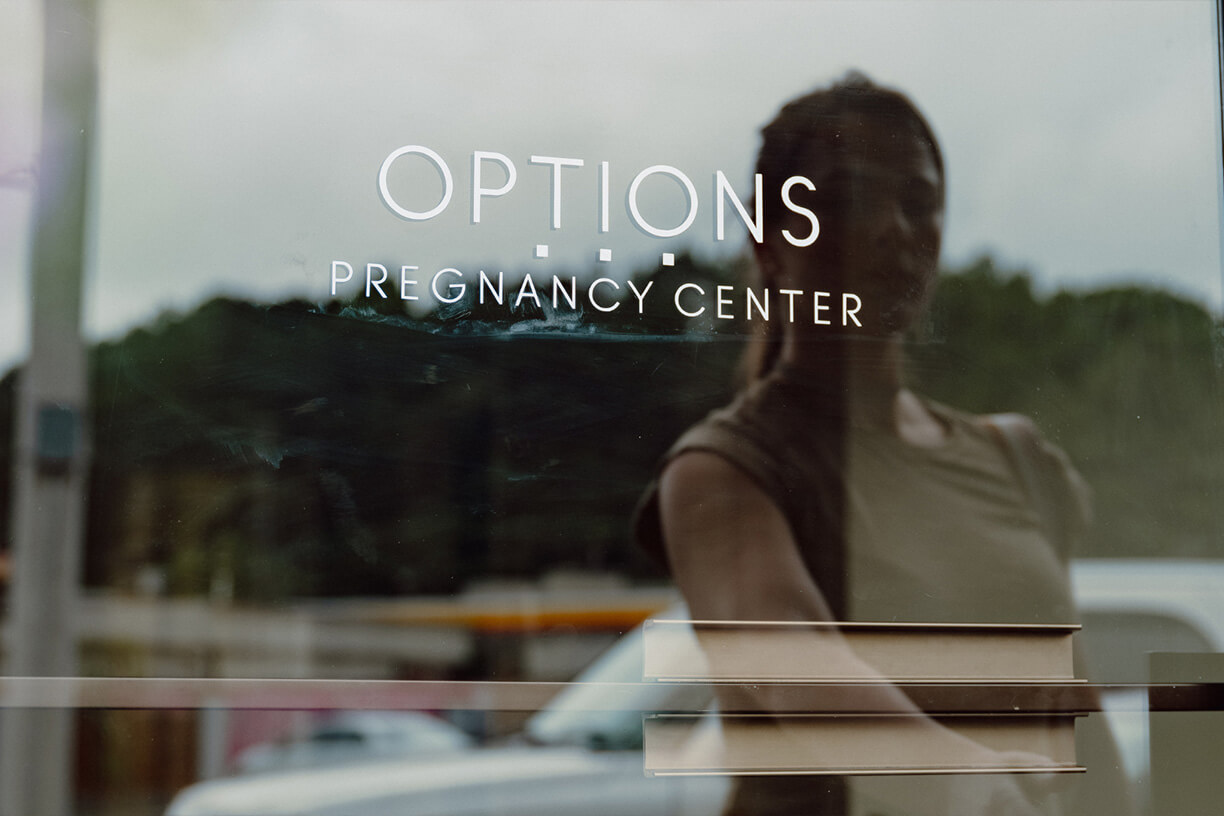 Woman standing outside pregnancy center with 'Options' sign