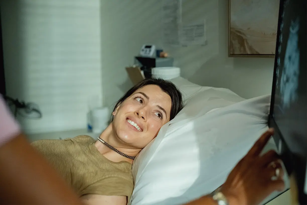 Pregnant woman smiling and looking at an ultrasound screen during a medical examination.